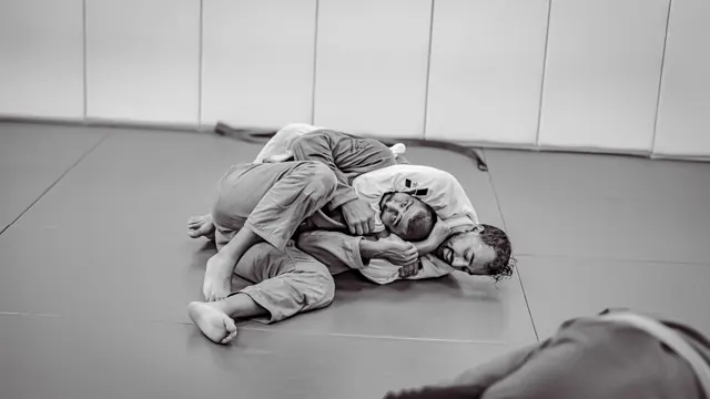 Two jiu-jitsu practitioners grappling on a mat in black and white.