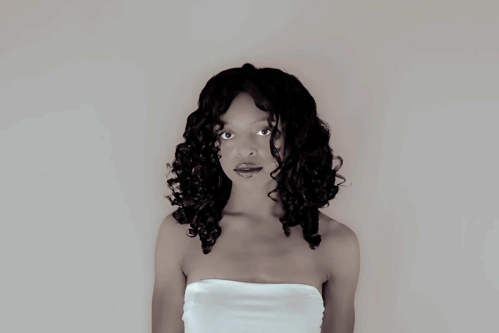 Black-and-white portrait of a woman with curls and a light strapless top.
