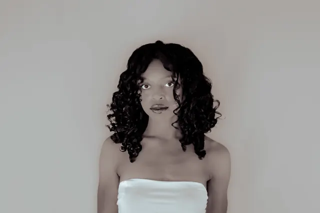Black-and-white portrait of a woman with curls and a light strapless top.