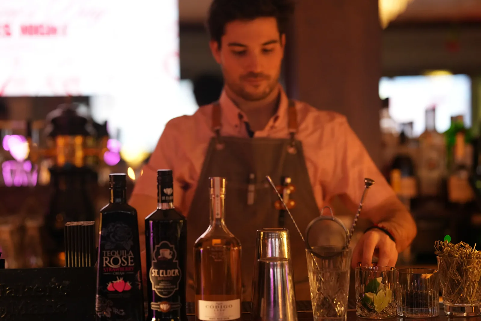 A bartender preparing drinks behind rows of bottles.