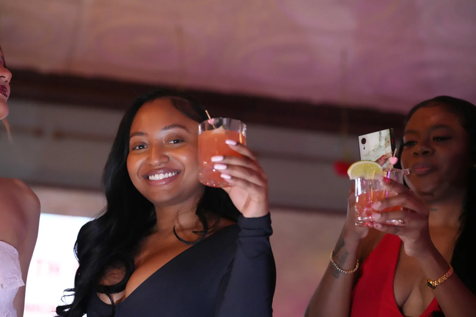 Two friends smiling and raising cocktails at a night out.
