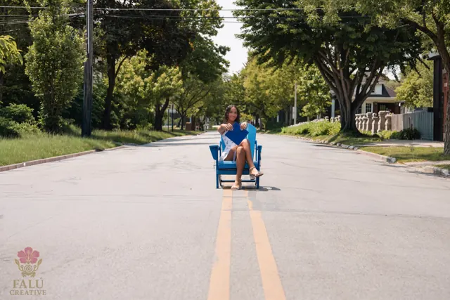A graduate seated in the center of an empty tree-lined street.