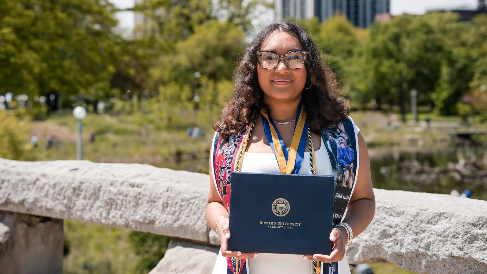 A graduate holding her diploma with Chicago in the distance.