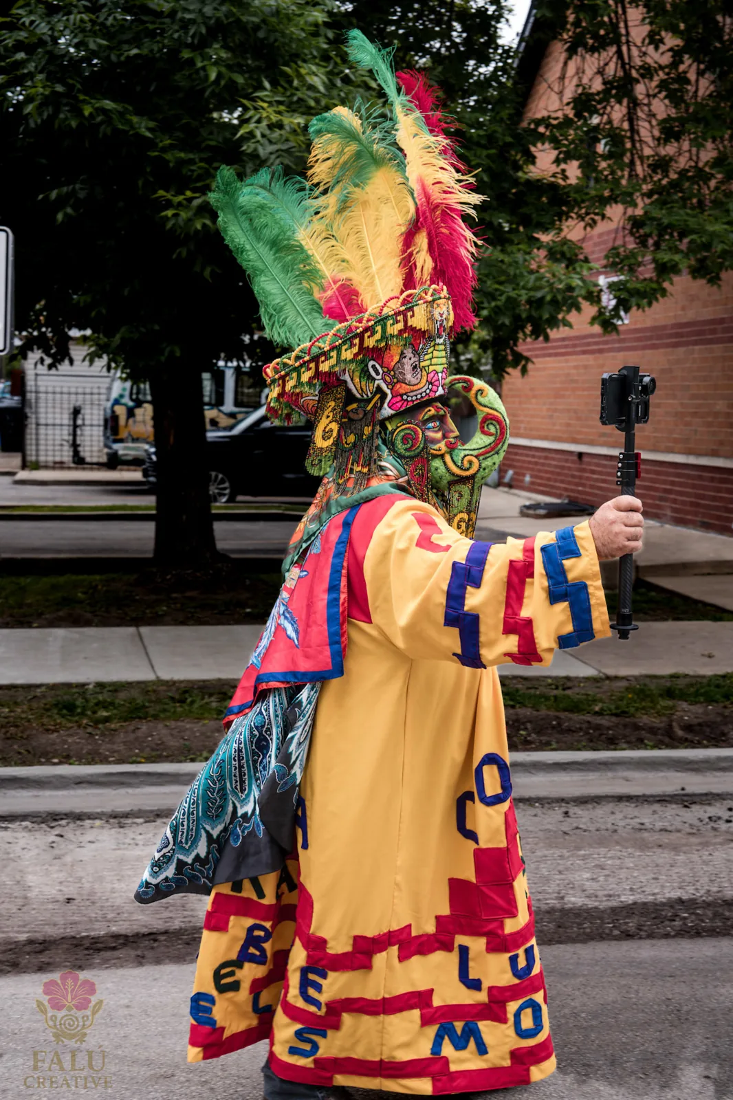A costumed parade performer in a bright red, yellow and green mask.